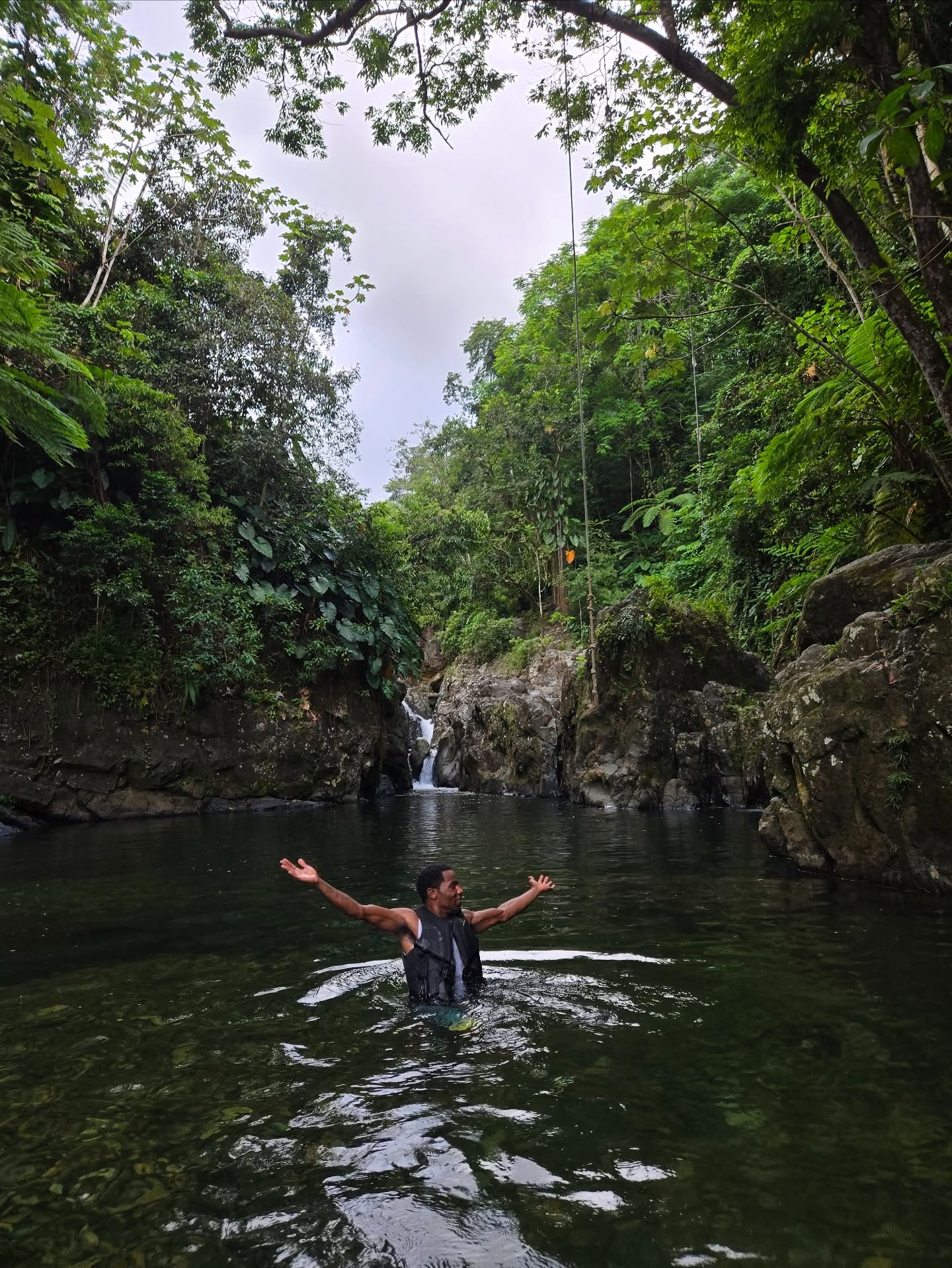Bobby, founder of Wizardly Solutions, standing arms-open in a jungle river pool beneath a waterfall — the freedom of financial liberation.